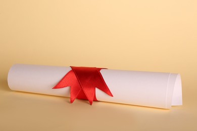 Rolled student's diploma with red ribbon on beige background