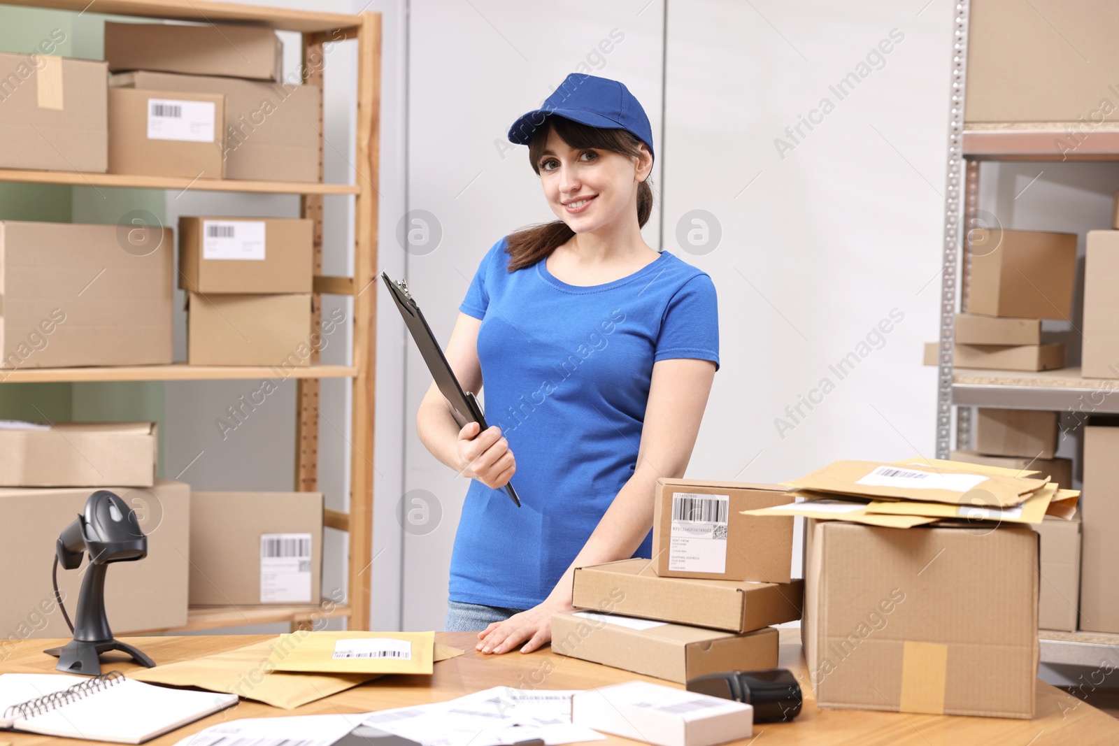 Photo of Parcel packing. Post office worker with clipboard at wooden table indoors