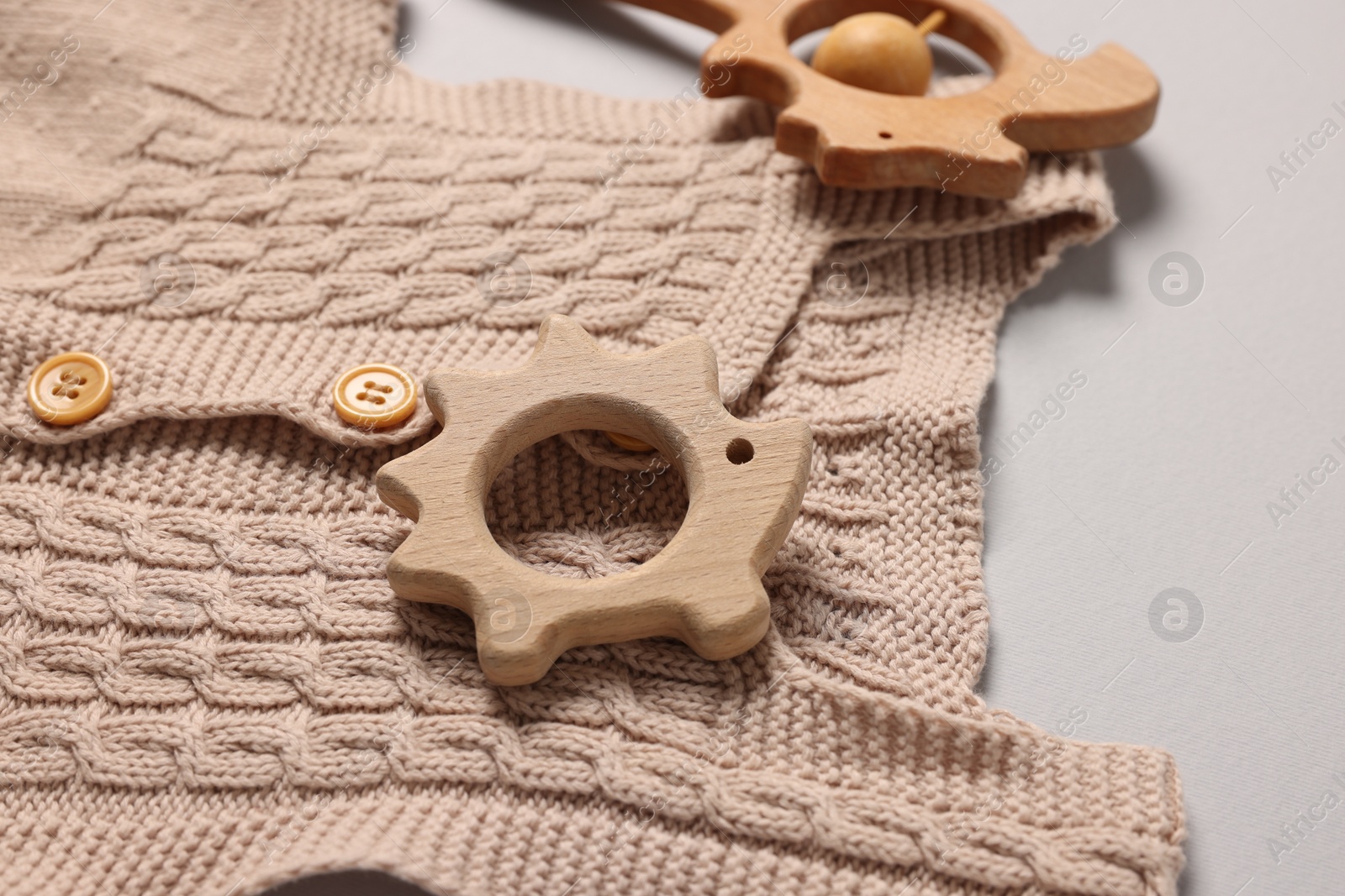 Photo of Baby accessories. Wooden rattle, teether and knitted cloth on grey background, closeup