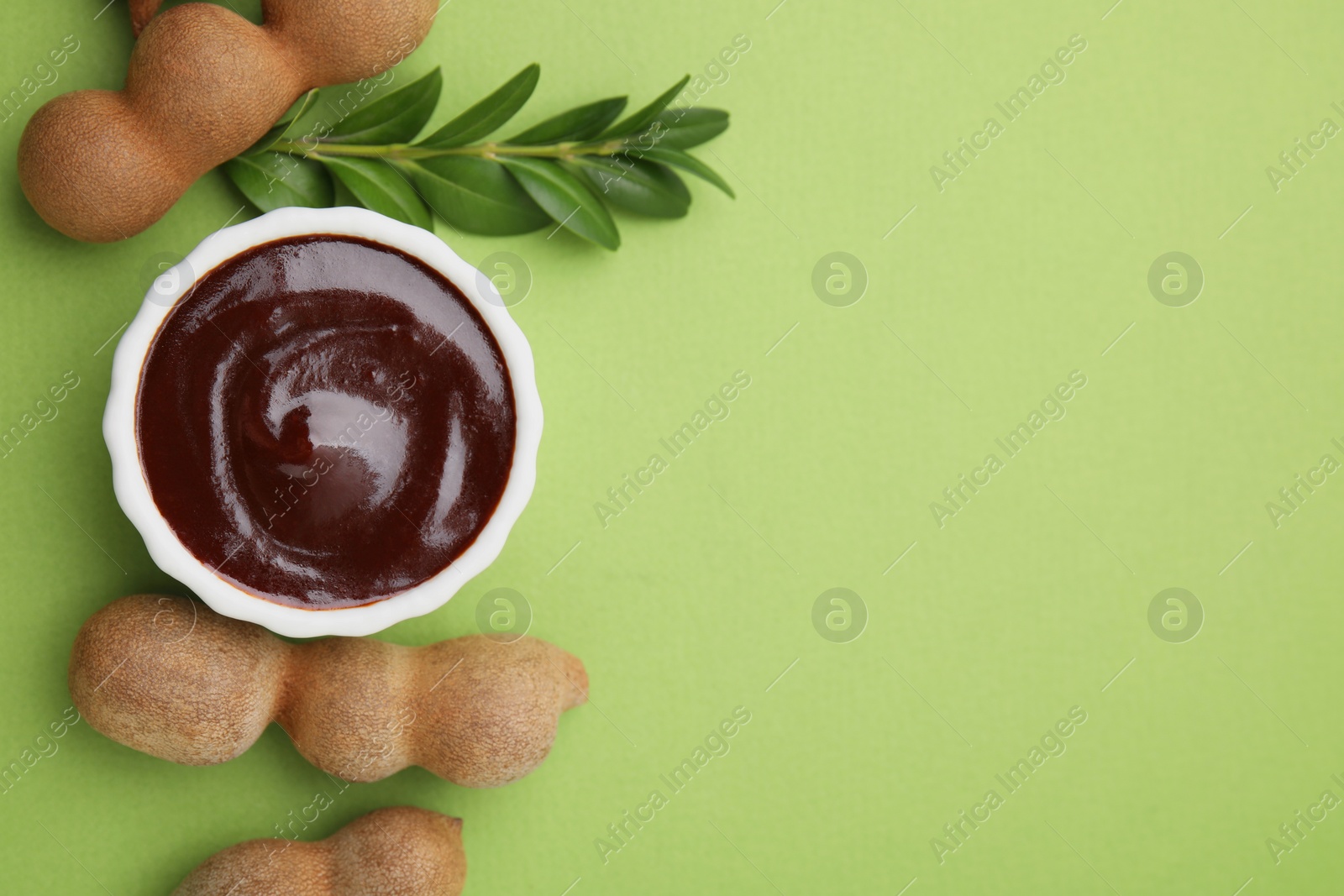 Bowl of tasty tamarind sauce, leaves and fresh pods on light green table, flat lay. Space for text Photo of Bowl of tasty tamarind sauce, leaves and fresh pods on light green table, flat lay. Space for text
