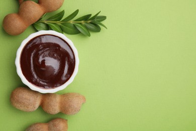 Photo of Bowl of tasty tamarind sauce, leaves and fresh pods on light green table, flat lay. Space for text