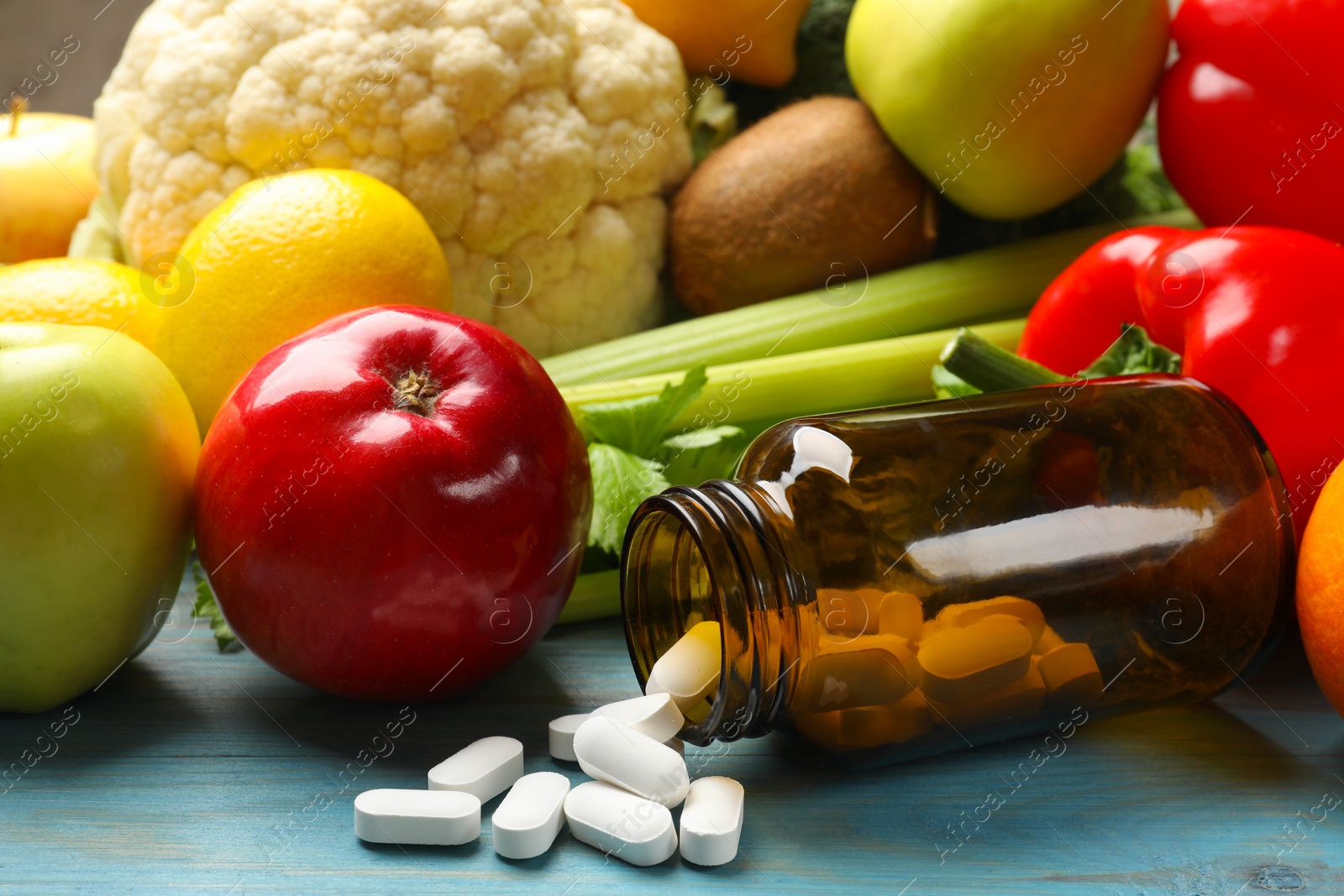 Photo of Dietary supplements. Overturned bottle with pills near food products on light blue wooden table