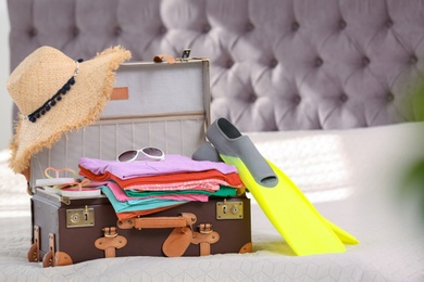 Photo of Vintage suitcase full of clothes on bed indoors