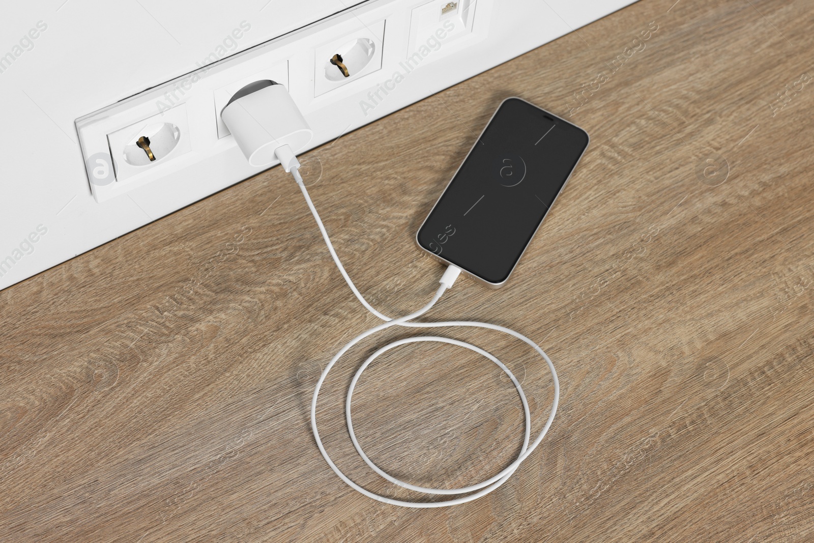 Photo of Modern smartphone charging on wooden table, above view