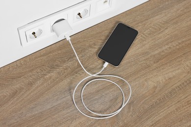 Modern smartphone charging on wooden table, above view