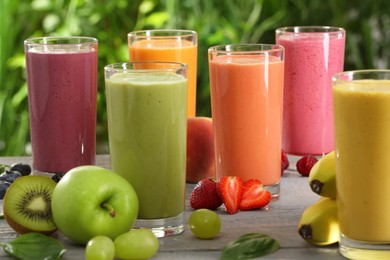 Photo of Many different delicious smoothies and ingredients on grey wooden table against blurred background