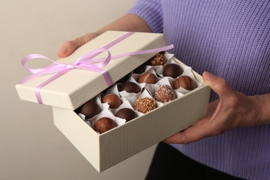 Woman holding box of delicious chocolate candies on light gray background, closeup