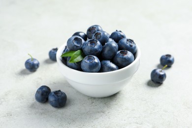 Photo of Bowl of fresh tasty blueberries on light grey table, closeup