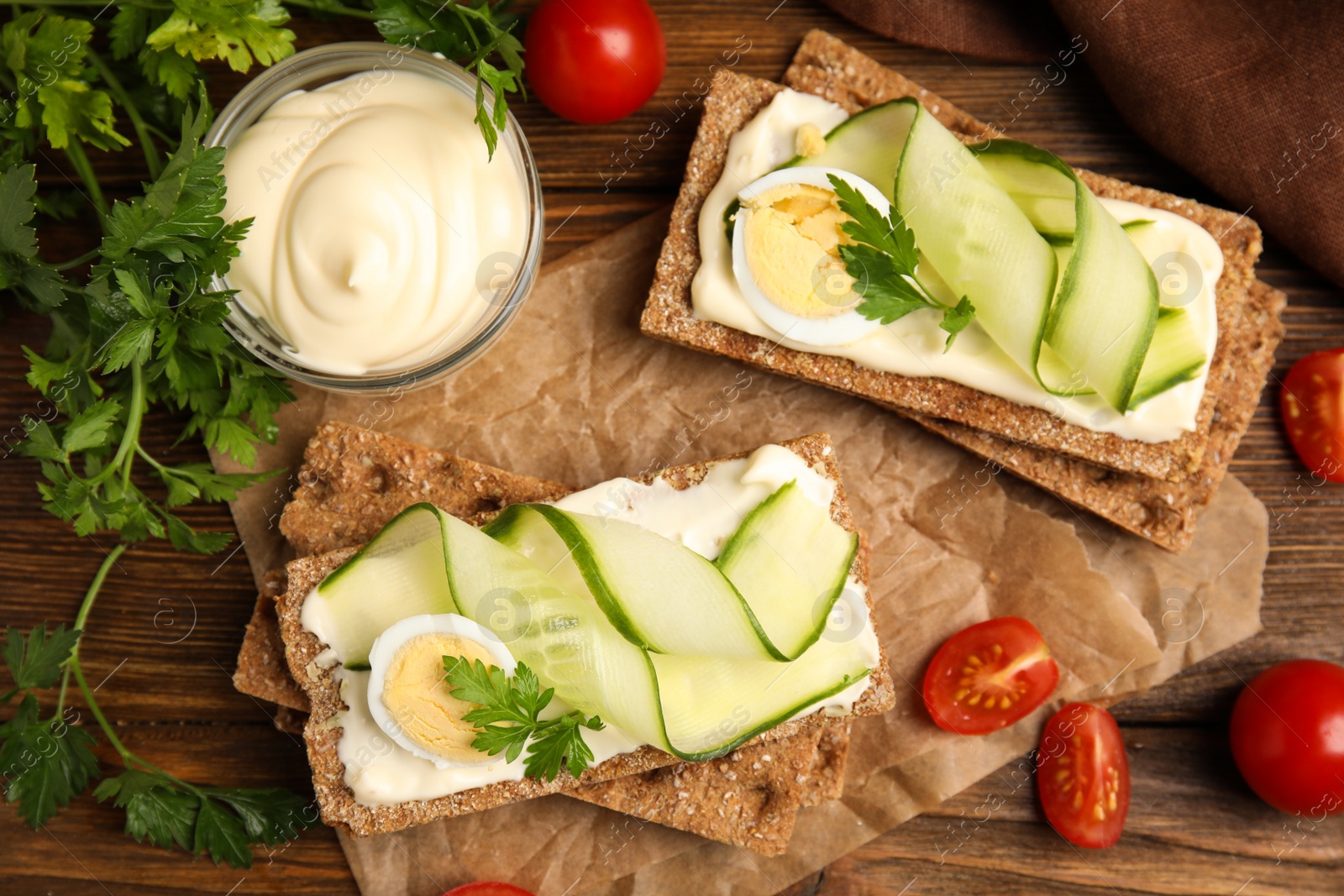 Photo of Fresh rye crispbreads with quail egg, cream cheese and cucumber slices on wooden table, flat lay