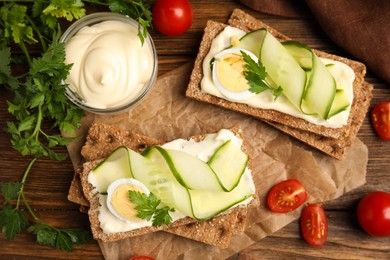 Fresh rye crispbreads with quail egg, cream cheese and cucumber slices on wooden table, flat lay