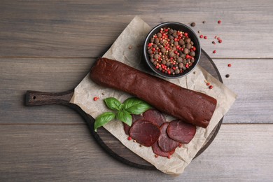 Delicious dry-cured beef basturma with basil and peppercorns on wooden table, flat lay