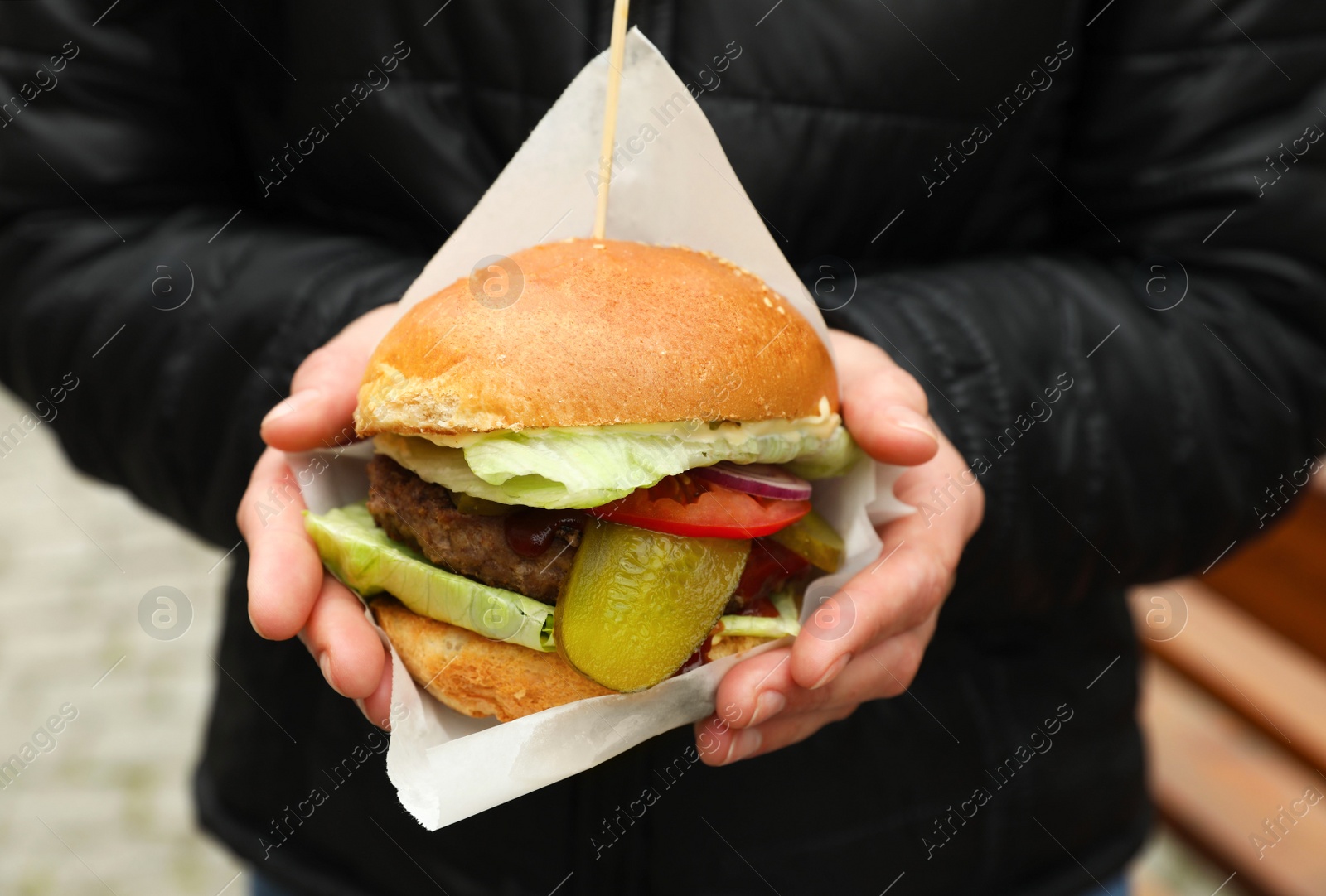 Photo of Woman holding fresh delicious burger outdoors, closeup. Street food