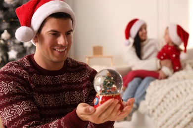 Man in Santa hat with snow globe at home