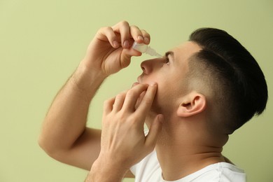 Man using eye drops on green background