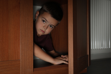 Photo of Sad little boy hiding in wardrobe. Domestic violence concept