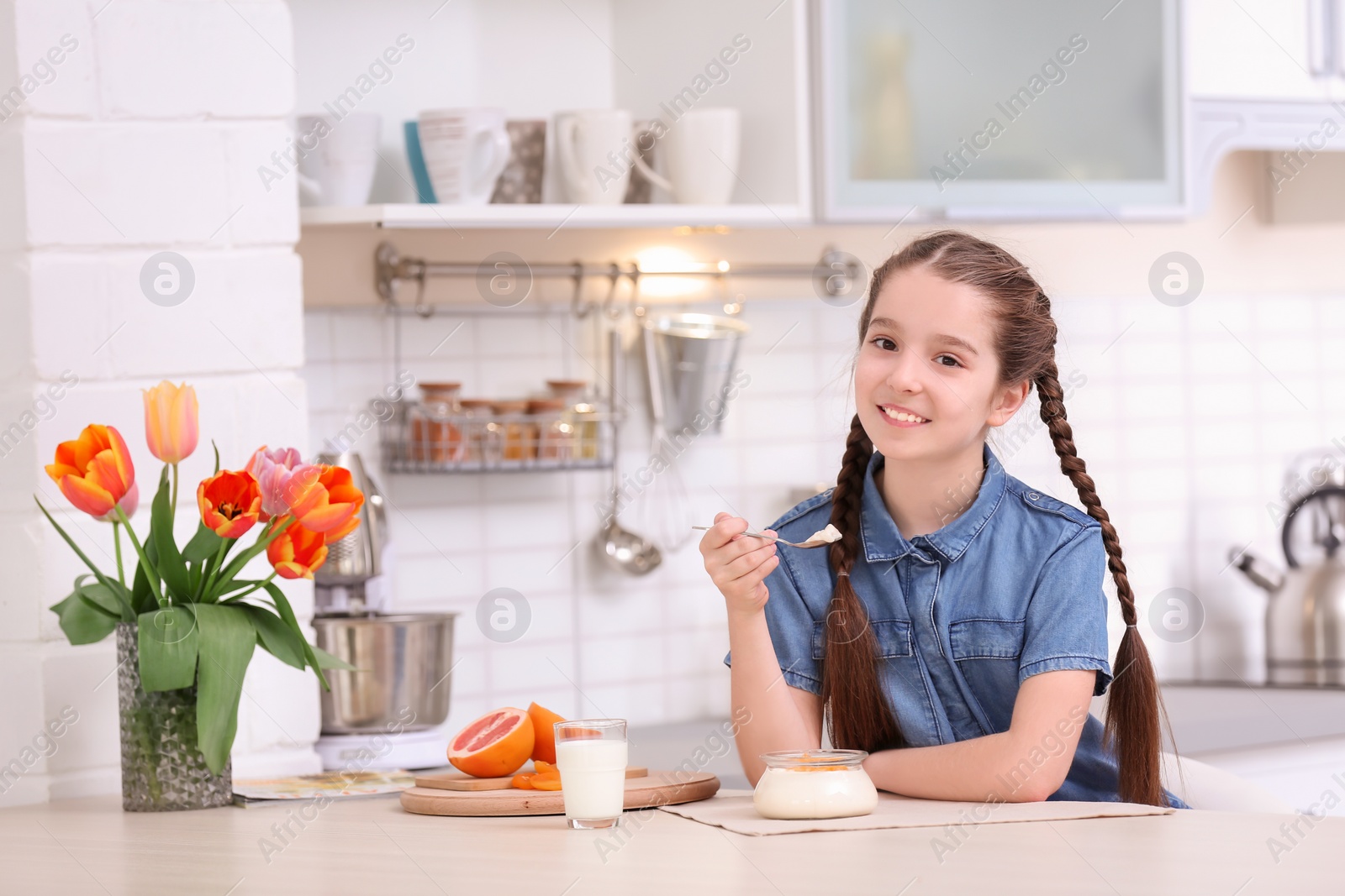 Photo of Cute girl eating tasty yogurt at table in kitchen