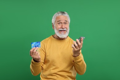 Photo of Stressful senior man with credit card and smartphone on green background. Be careful - fraud