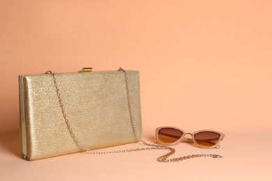 Stylish woman's bag and sunglasses on pale pink background