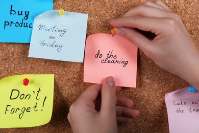 Woman pinning paper note with phrase Do The Cleaning to cork board, closeup