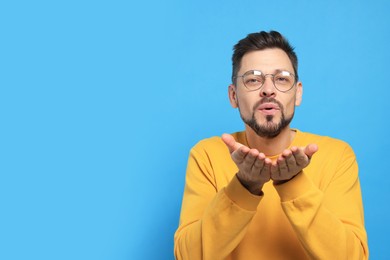 Handsome man blowing kiss on light blue background. Space for text