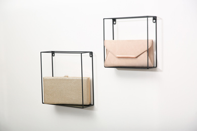 Photo of Metal shelves with stylish woman's bags on white wall