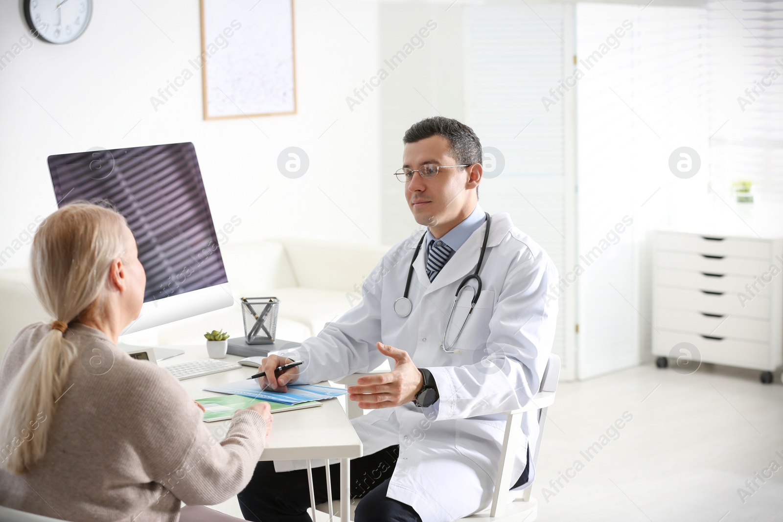 Photo of Doctor consulting patient at desk in clinic