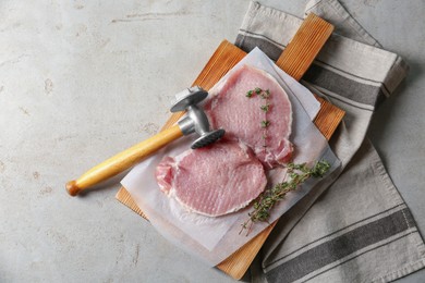 Photo of Cooking schnitzel. Raw pork chops, thyme and meat mallet on grey table, top view with space for text