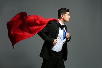 Photo of Businessman in superhero cape taking suit off on grey background