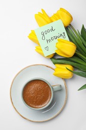 Photo of Cup of aromatic coffee, beautiful yellow tulips and Good Morning note on white background, flat lay