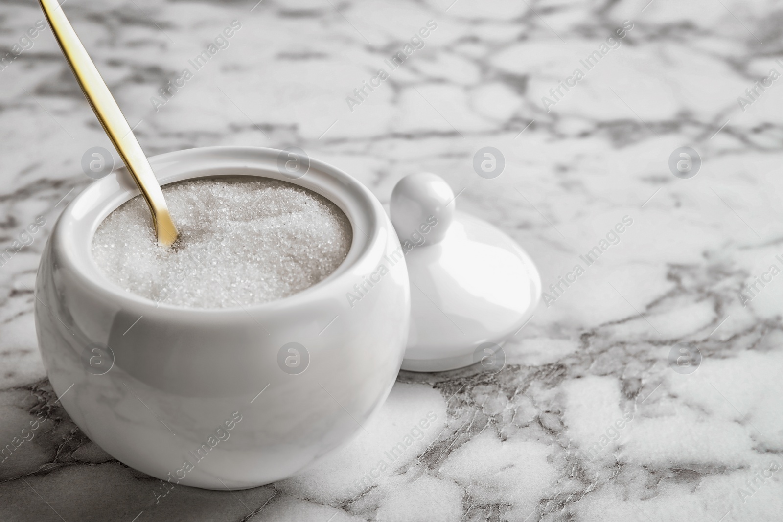 Photo of Granulated sugar in bowl on white marble table. Space for text