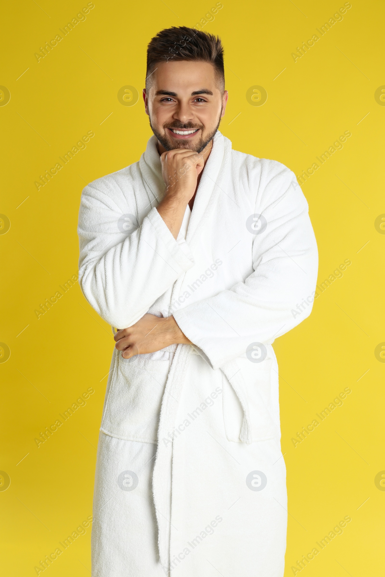 Photo of Happy young man in bathrobe on yellow background
