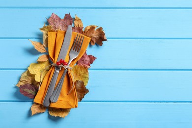 Photo of Thanksgiving table setting. Cutlery, napkin, autumn leaves and berries on light blue wooden background, top view, Space for text