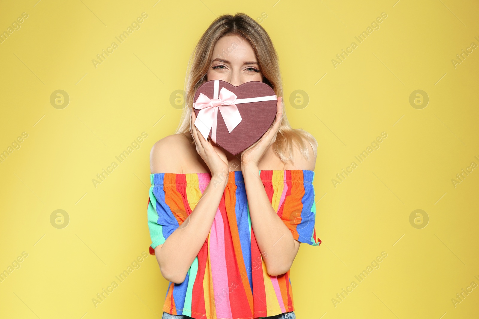 Photo of Portrait of beautiful girl with heart shaped gift box on yellow background. International Women's Day