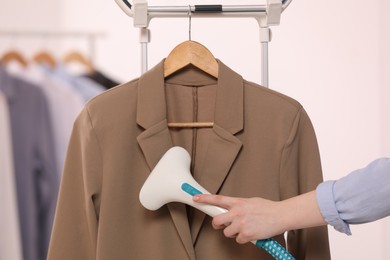 Woman steaming jacket on hanger in room, closeup