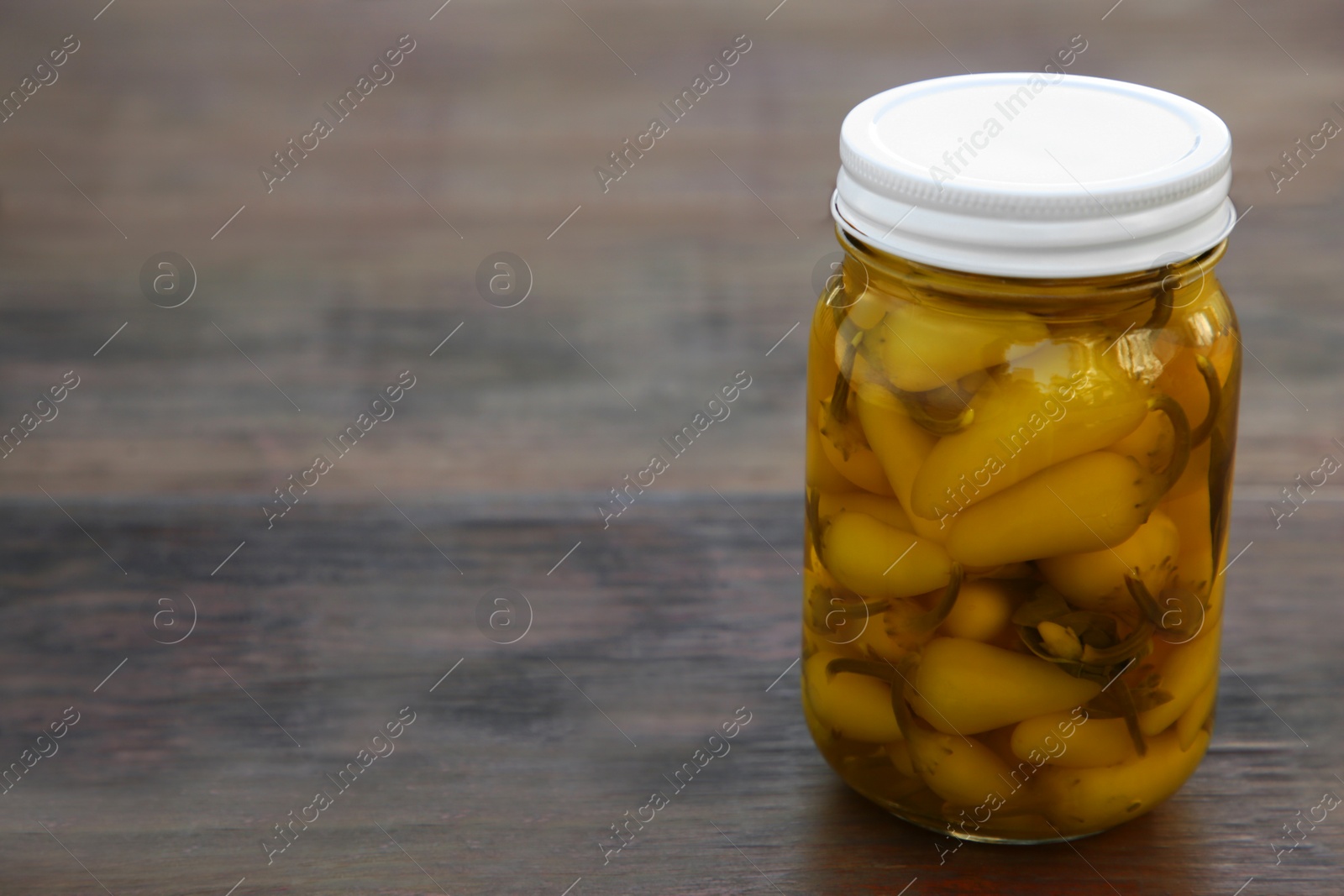 Photo of Glass jar of pickled yellow jalapeno peppers on wooden table. Space for text