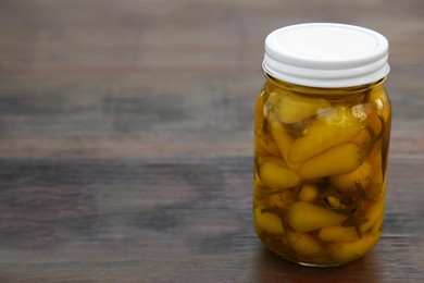 Glass jar of pickled yellow jalapeno peppers on wooden table. Space for text