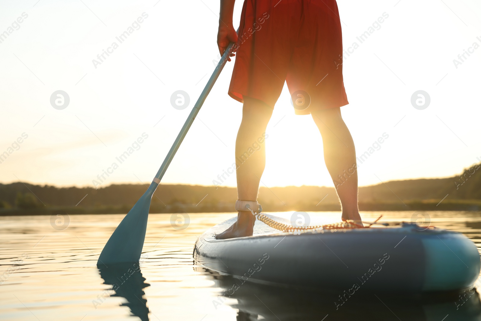 Photo of Man paddle boarding on SUP board in river at sunset, closeup