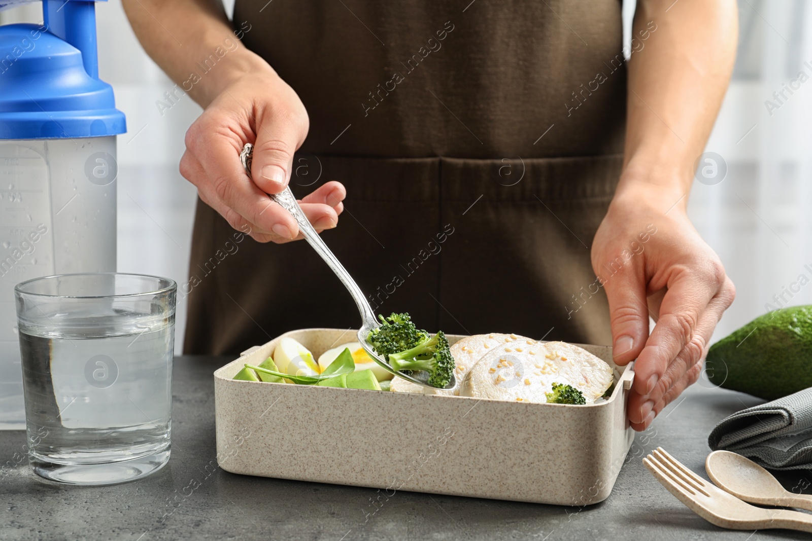 Photo of Woman putting natural protein food into container on gray table, closeup