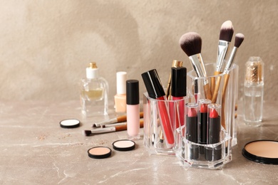 Photo of Lipstick holder with different makeup products on table against color background. Space for text