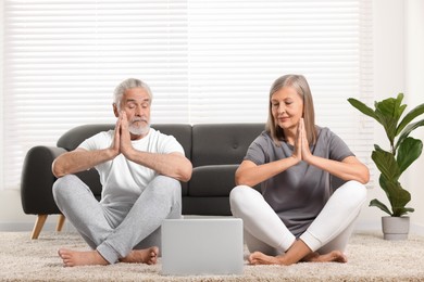 Photo of Senior couple practicing yoga with laptop at home