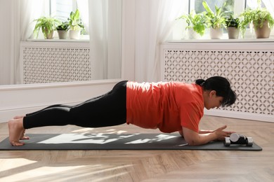 Photo of Overweight mature woman doing plank exercise at home