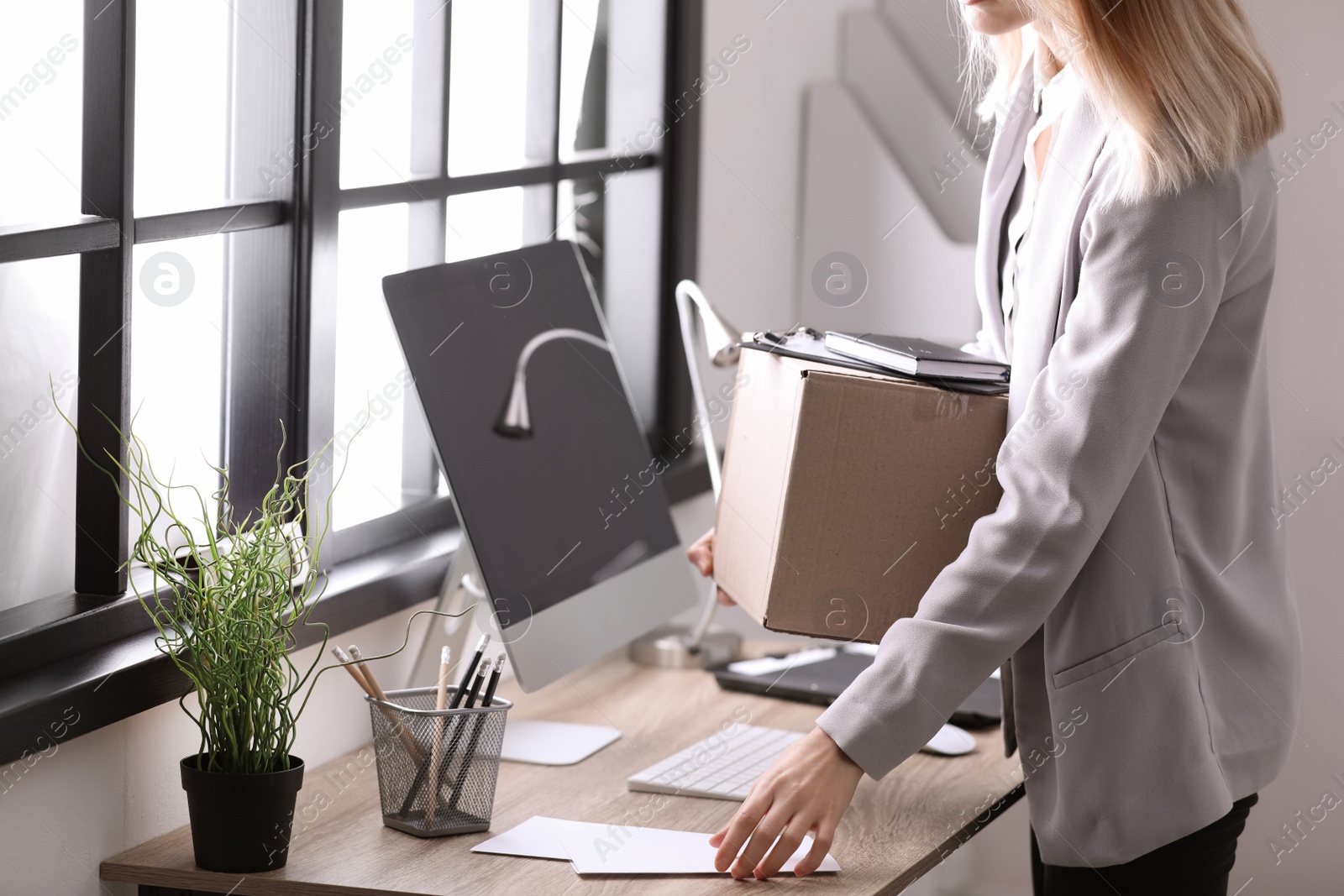 Photo of Young woman holding moving box with office stuff indoors, closeup