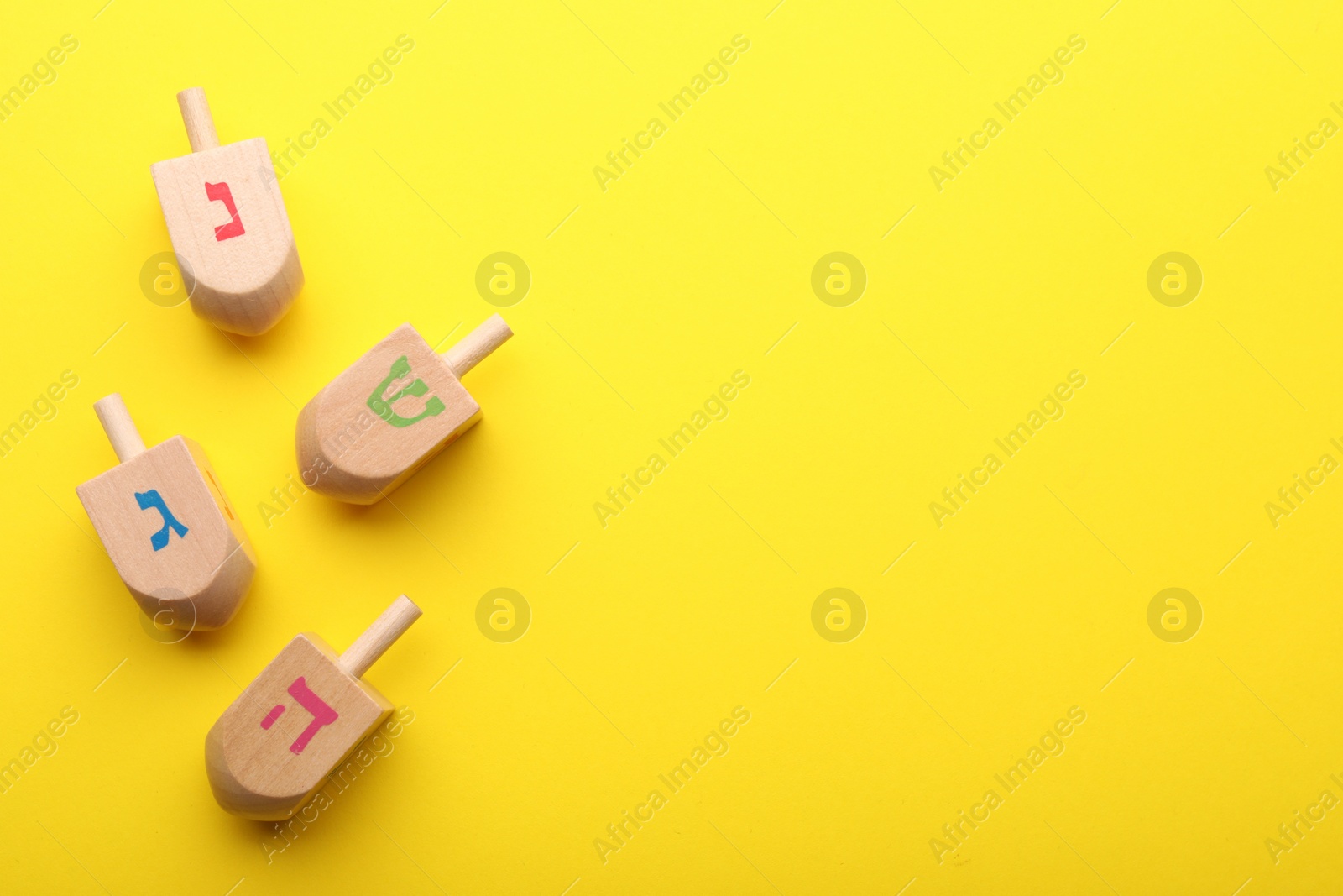 Photo of Wooden dreidels on yellow background, flat lay with space for text. Traditional Hanukkah game