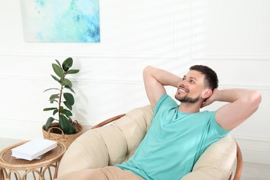 Photo of Handsome man relaxing in papasan chair at home, space for text