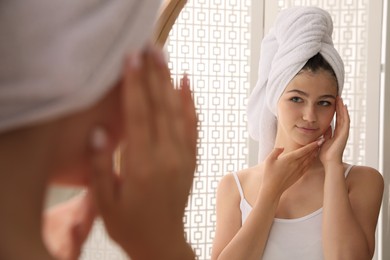 Beautiful teenage girl with towel near mirror in bathroom