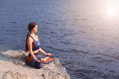 Teenage girl meditating on cliff near river at sunrise. Practicing yoga