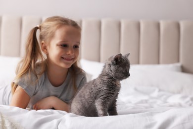 Photo of Cute little girl with kitten on bed at home. Childhood pet
