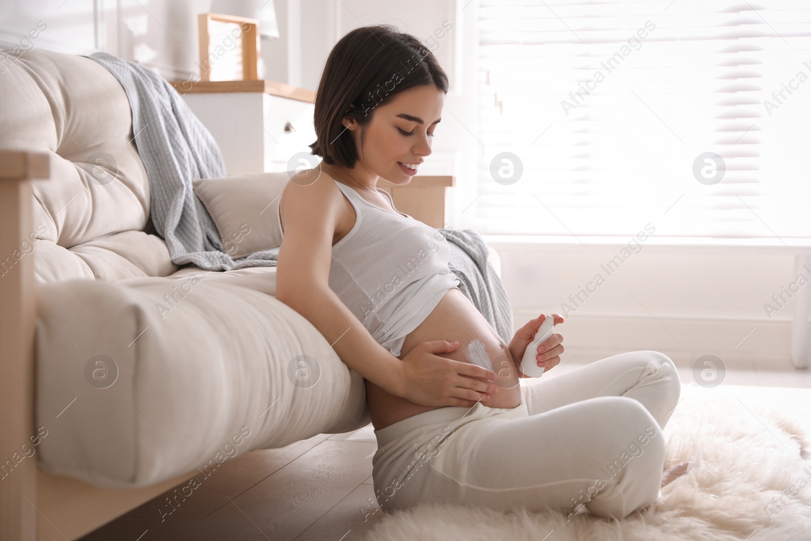 Photo of Young pregnant woman with cosmetic product at home