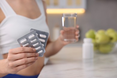 Photo of Weight loss. Woman with pills and glass of water at table indoors, closeup. Space for text