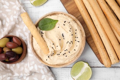 Photo of Delicious hummus with grissini sticks served on white wooden table, flat lay